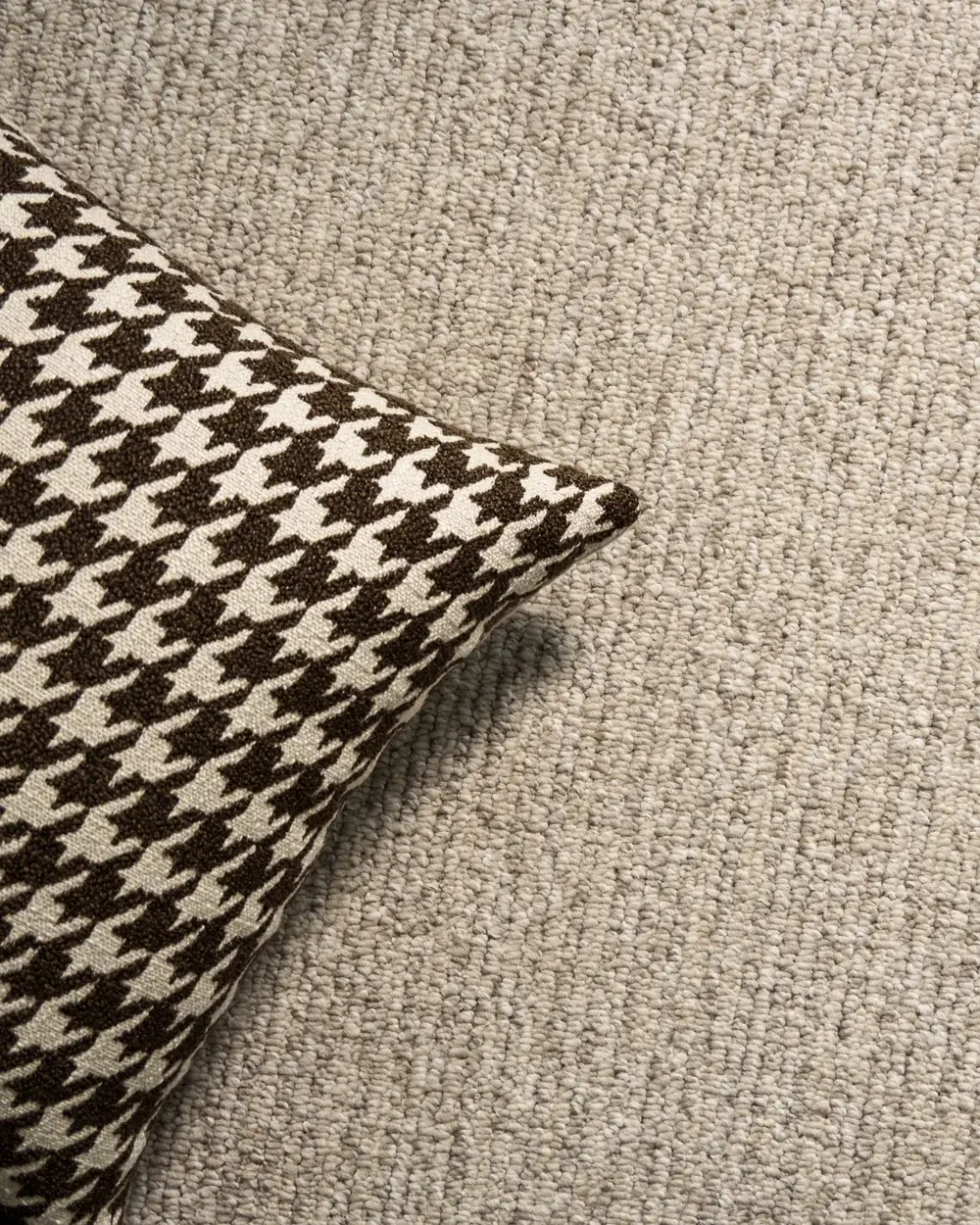 Close-up of a textured neutral carpet with a cushion resting on it