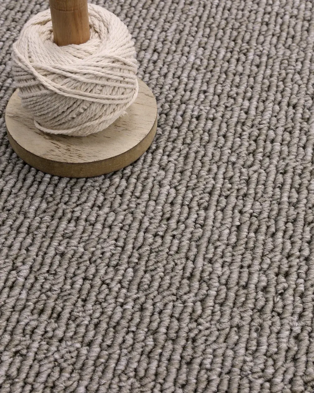 Spool of natural yarn resting on a textured neutral carpet
