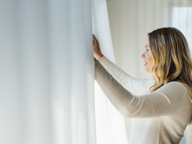 A hand resting against a sheer curtain at a window