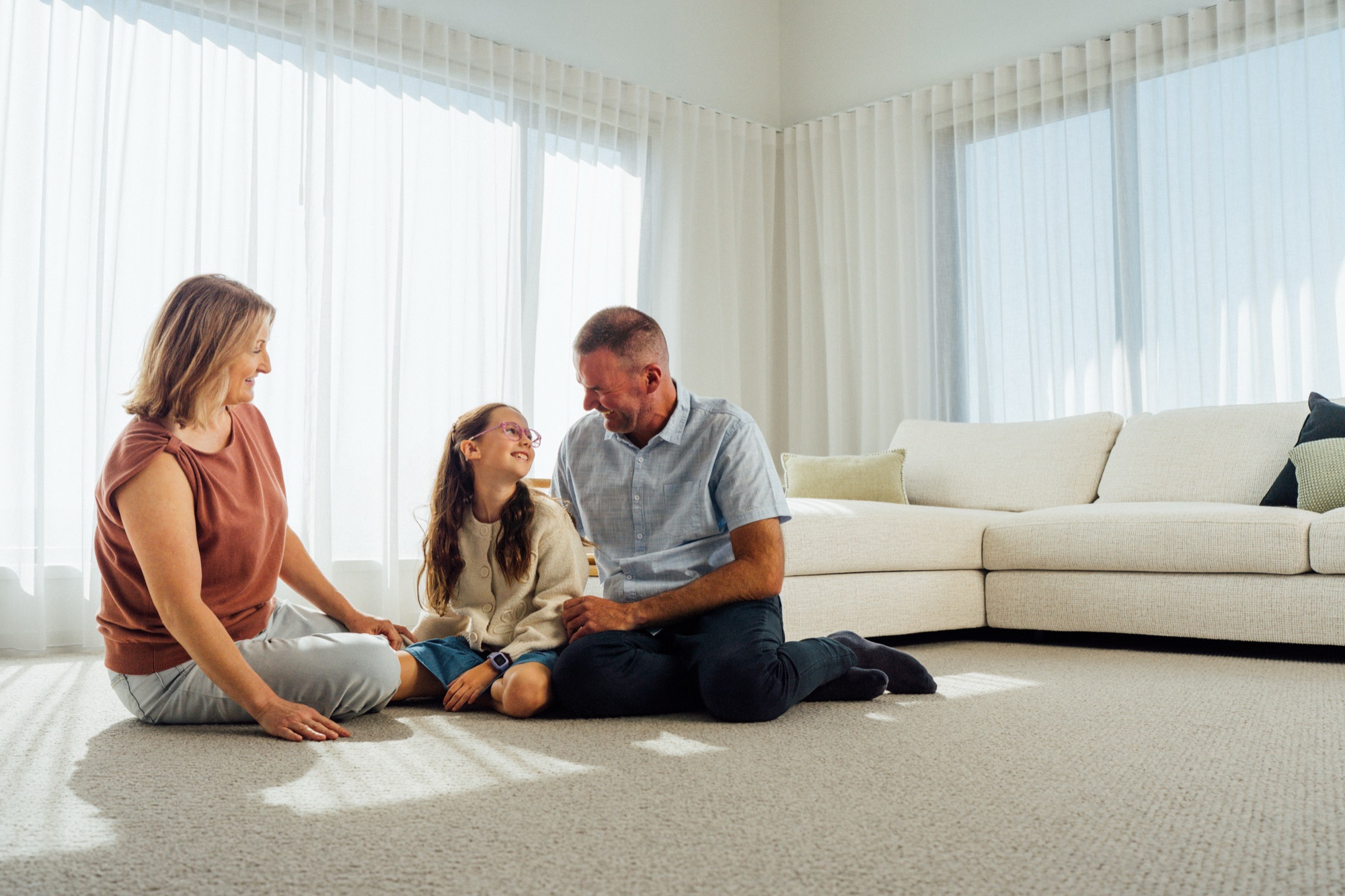 A family sitting together on the carpet of their living room in afternoon light