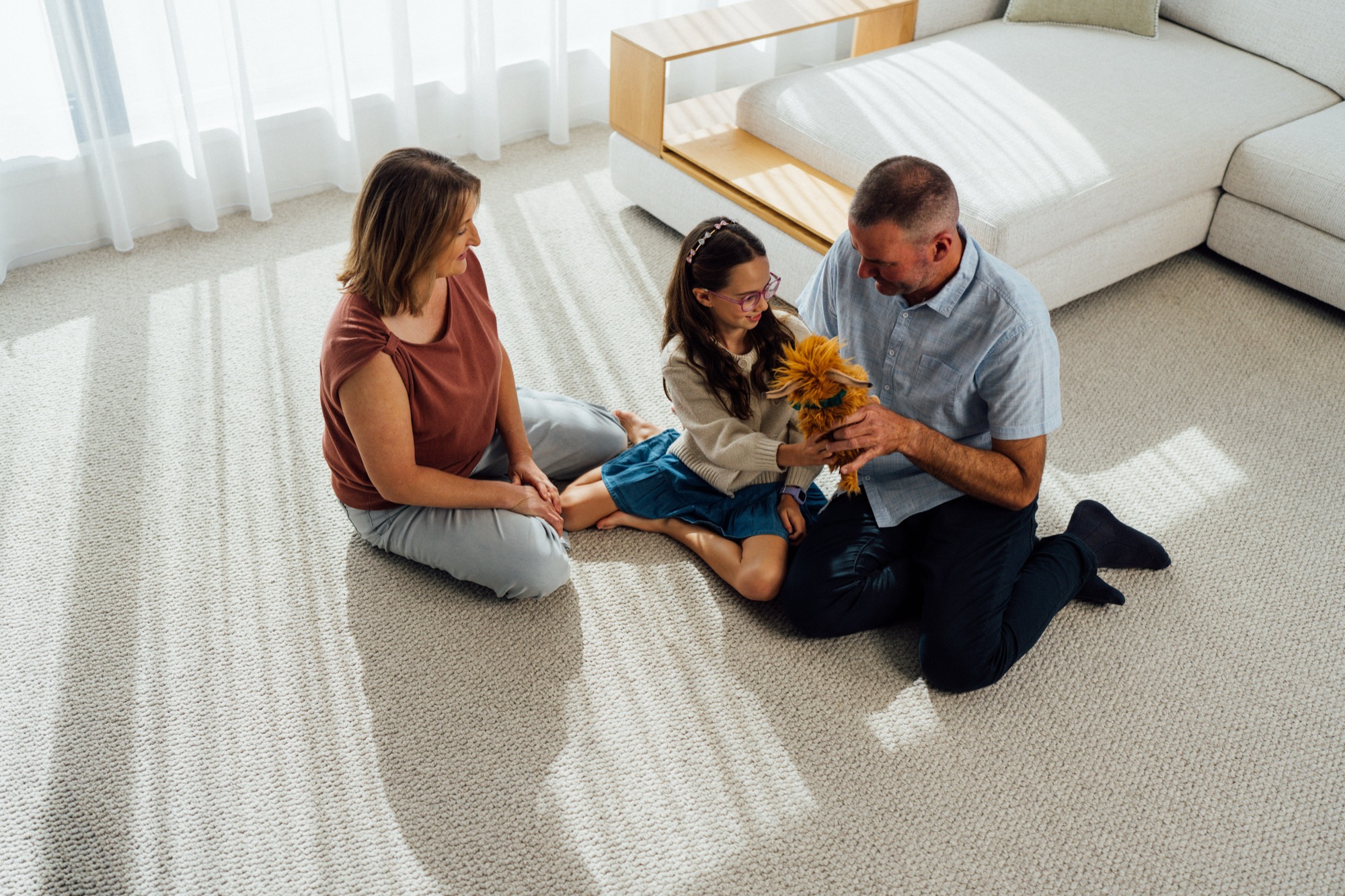A family sitting together on pale carpet in a bright living room