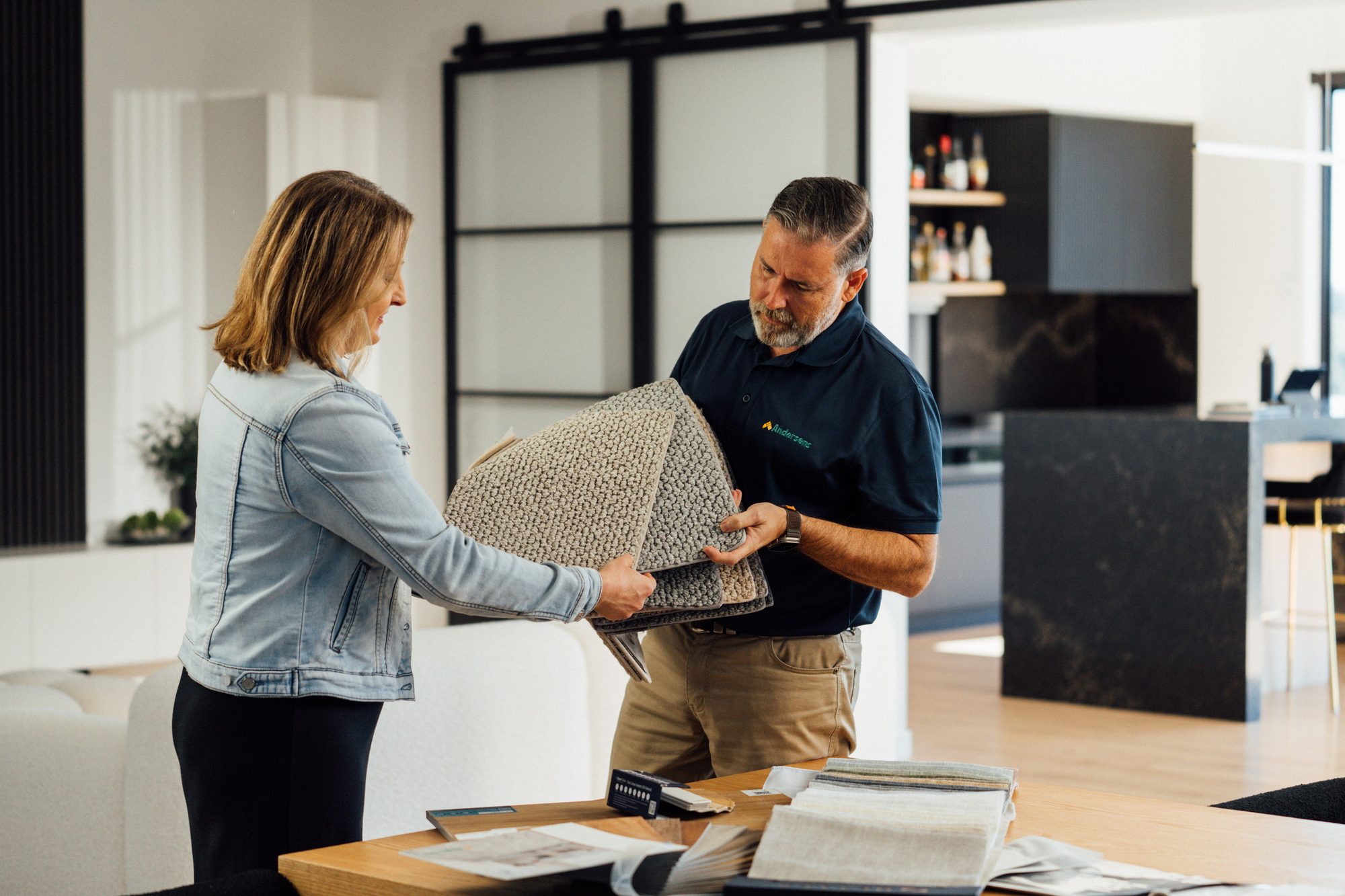 An Andersens consultant handing a folded carpet sample to a customer in her living room