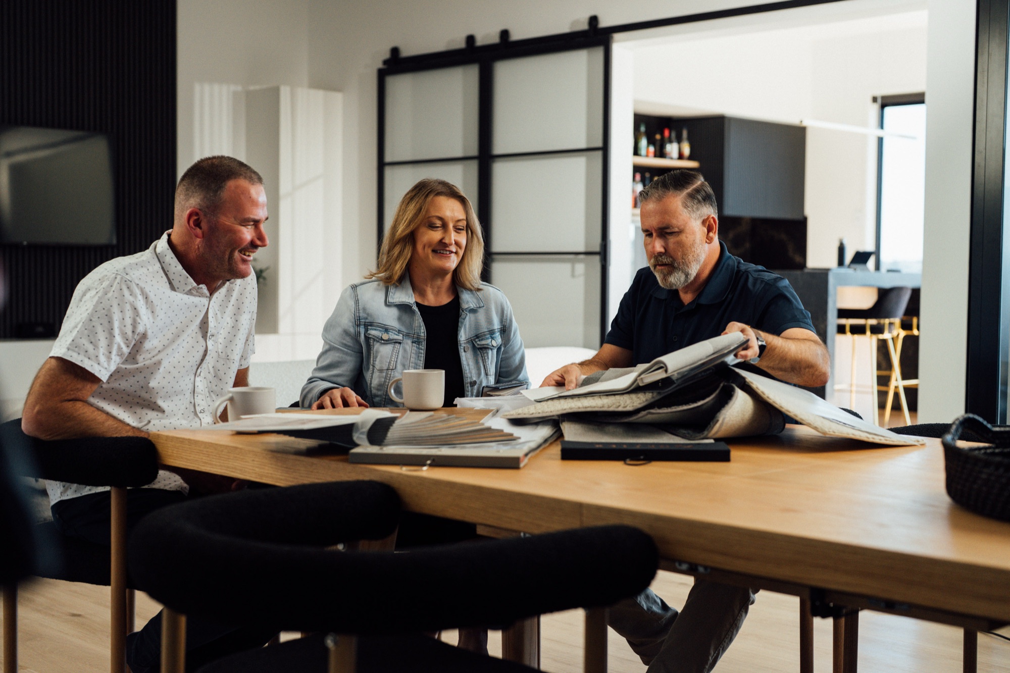 An Andersens consultant going through sample books with two customers at their dining table