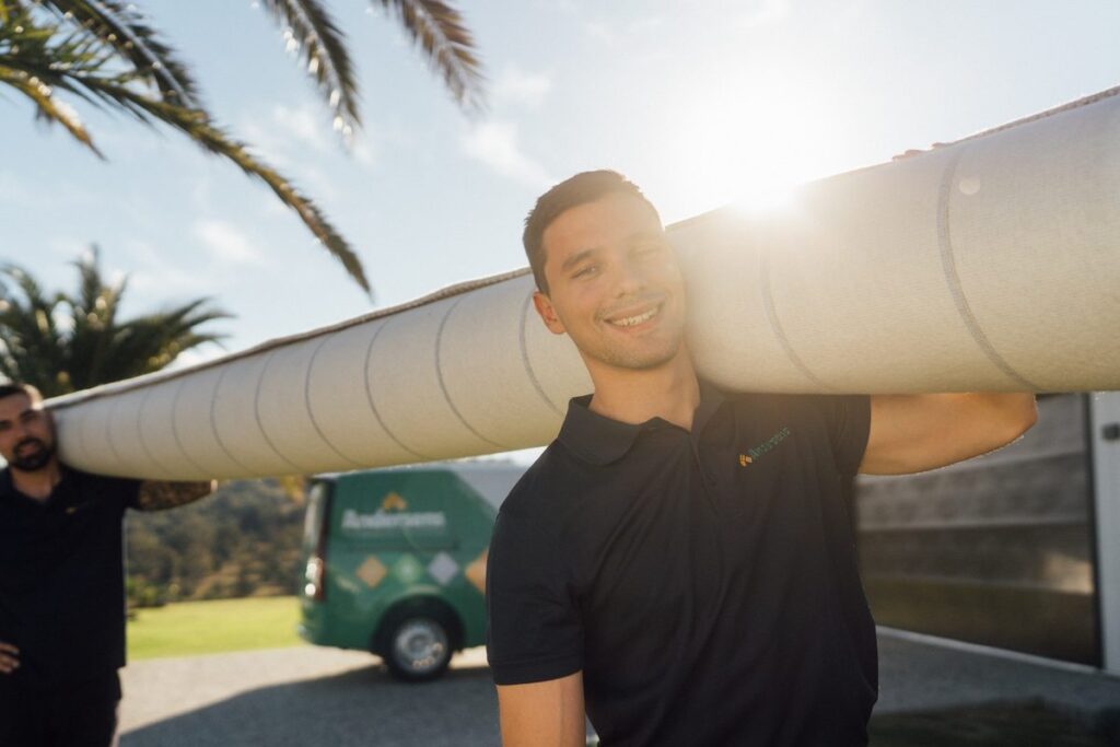Andersens installer carrying a roll of carpet beside a branded van