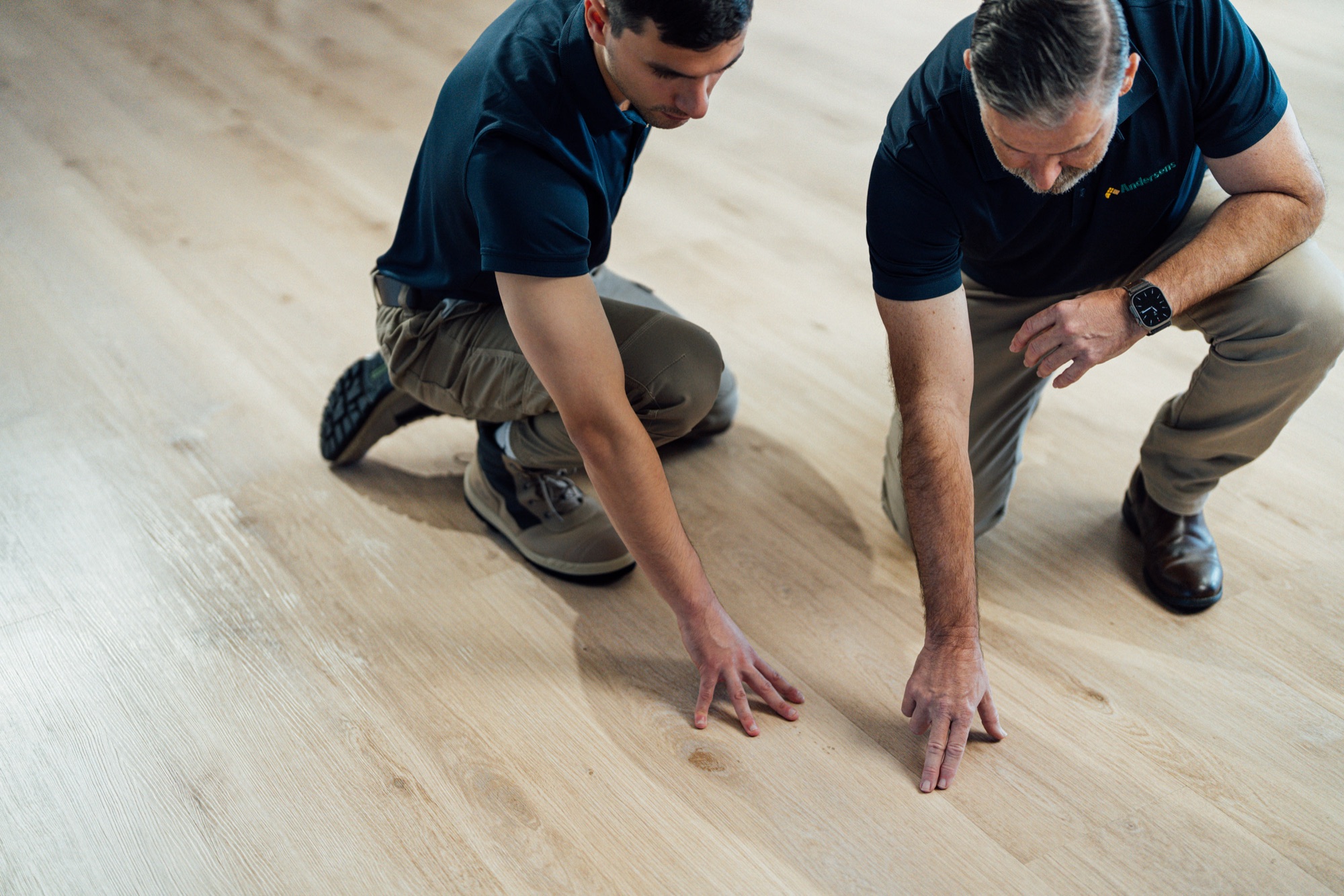 Two Andersens installers kneeling to work on a timber-look floor in a home