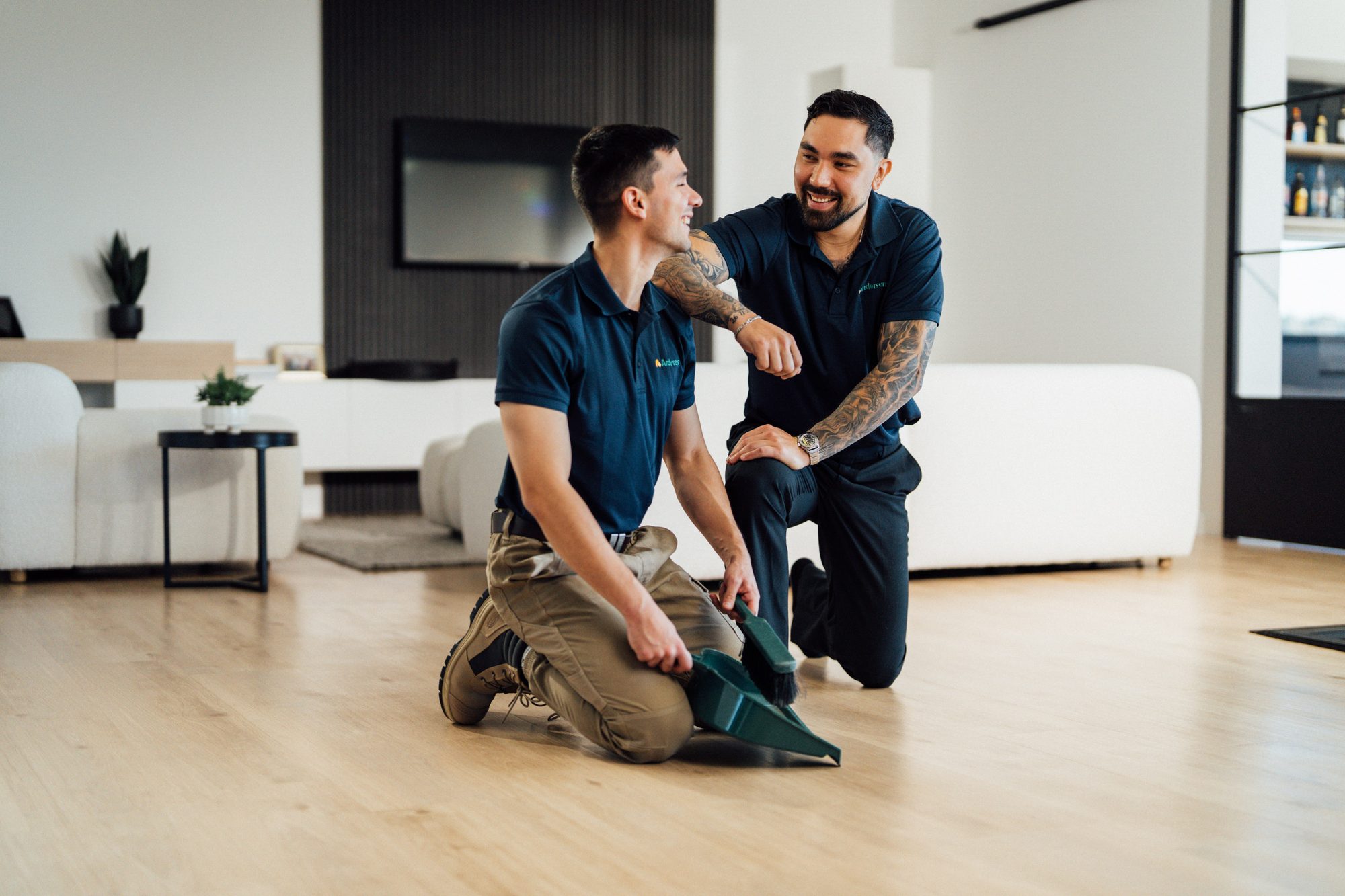 Two Andersens installers kneeling to fit a timber-look floor in a bright living room