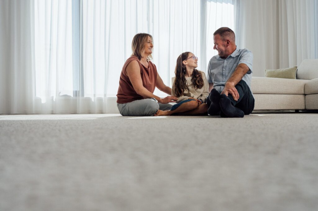 A living room with carpet and sheer curtains in afternoon daylight