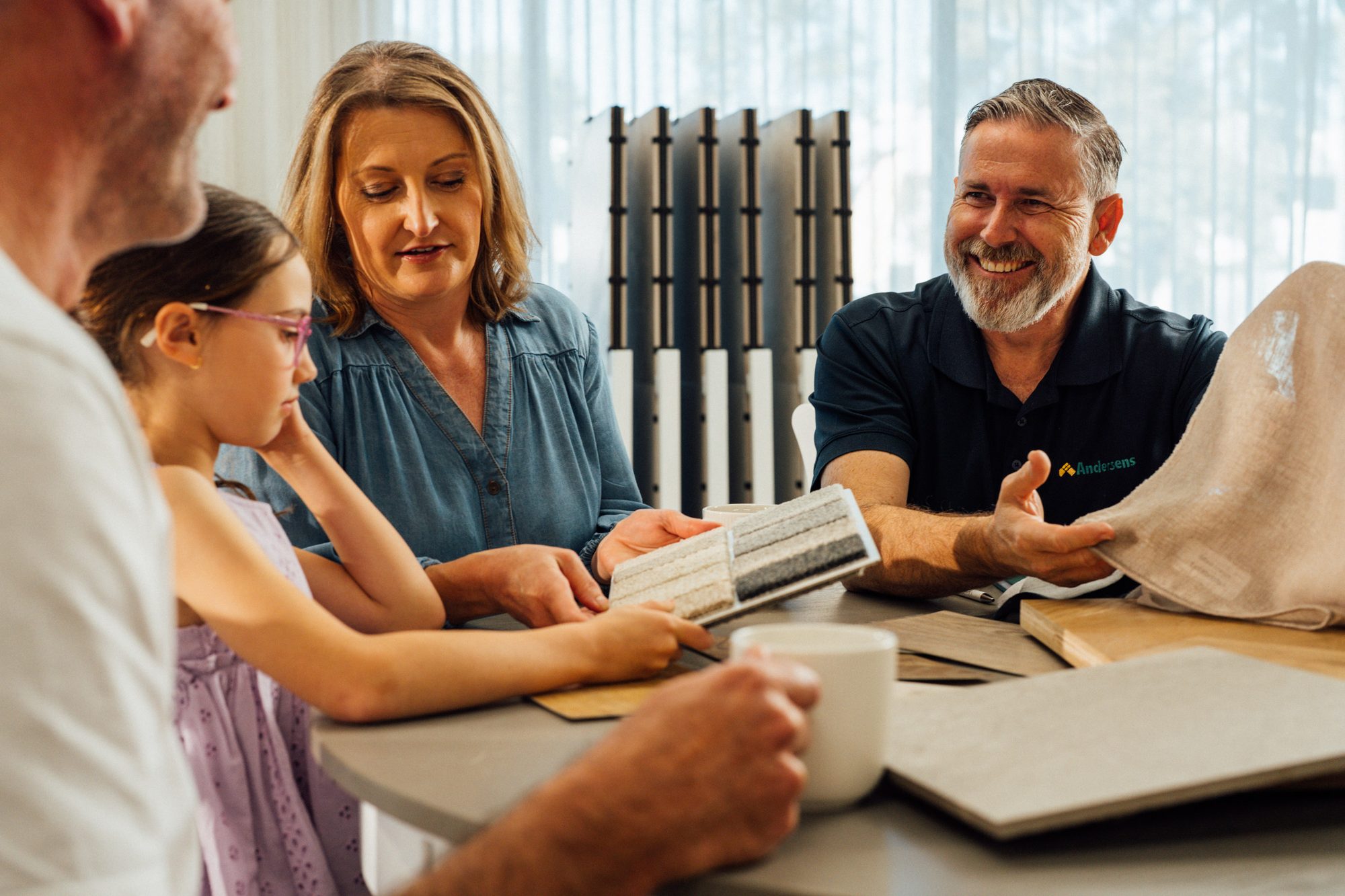 An Andersens consultant showing carpet, tile and timber samples to a family around a table