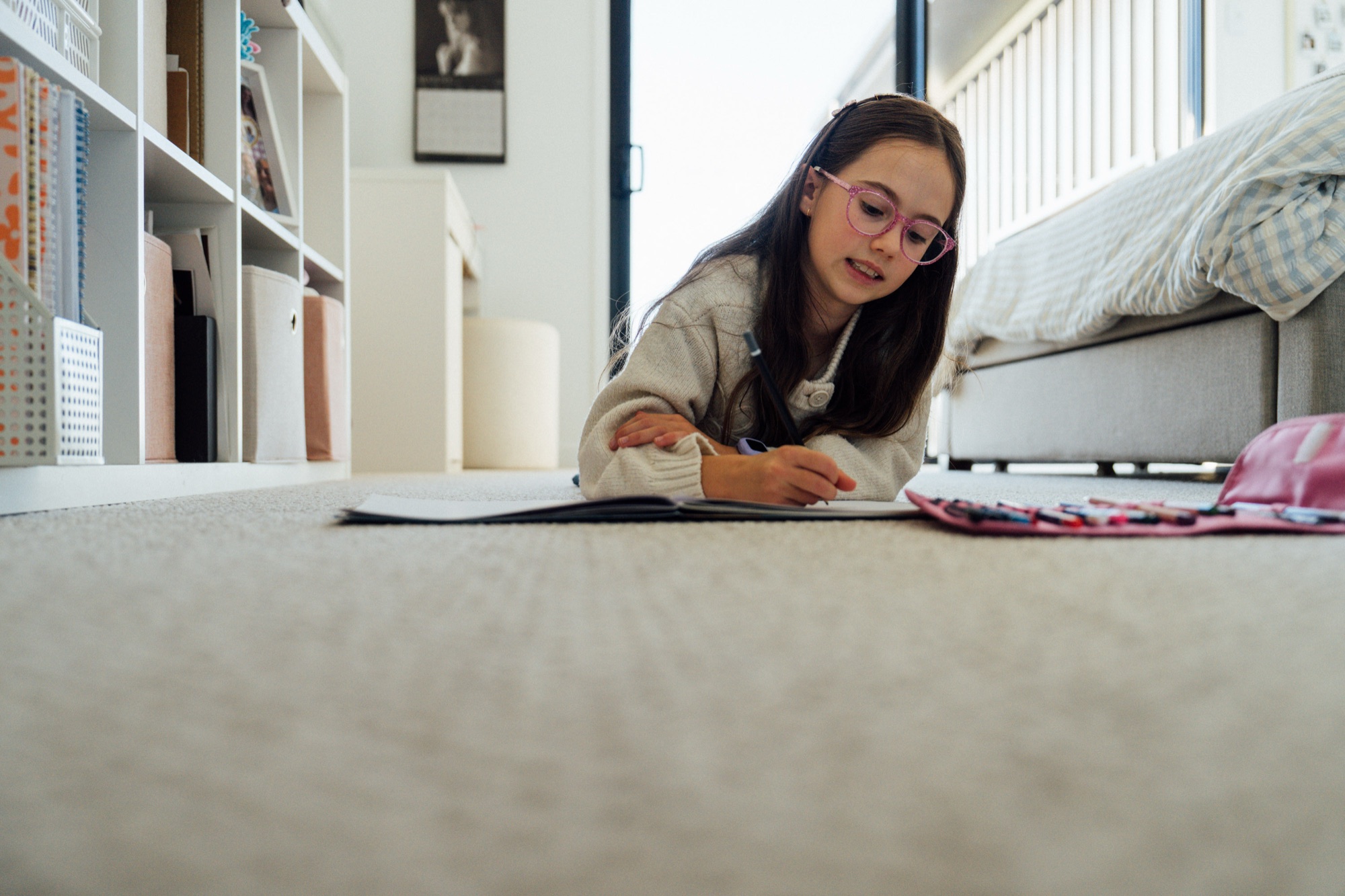 A woman lying on the carpet of her living room reading, with a bookshelf behind her