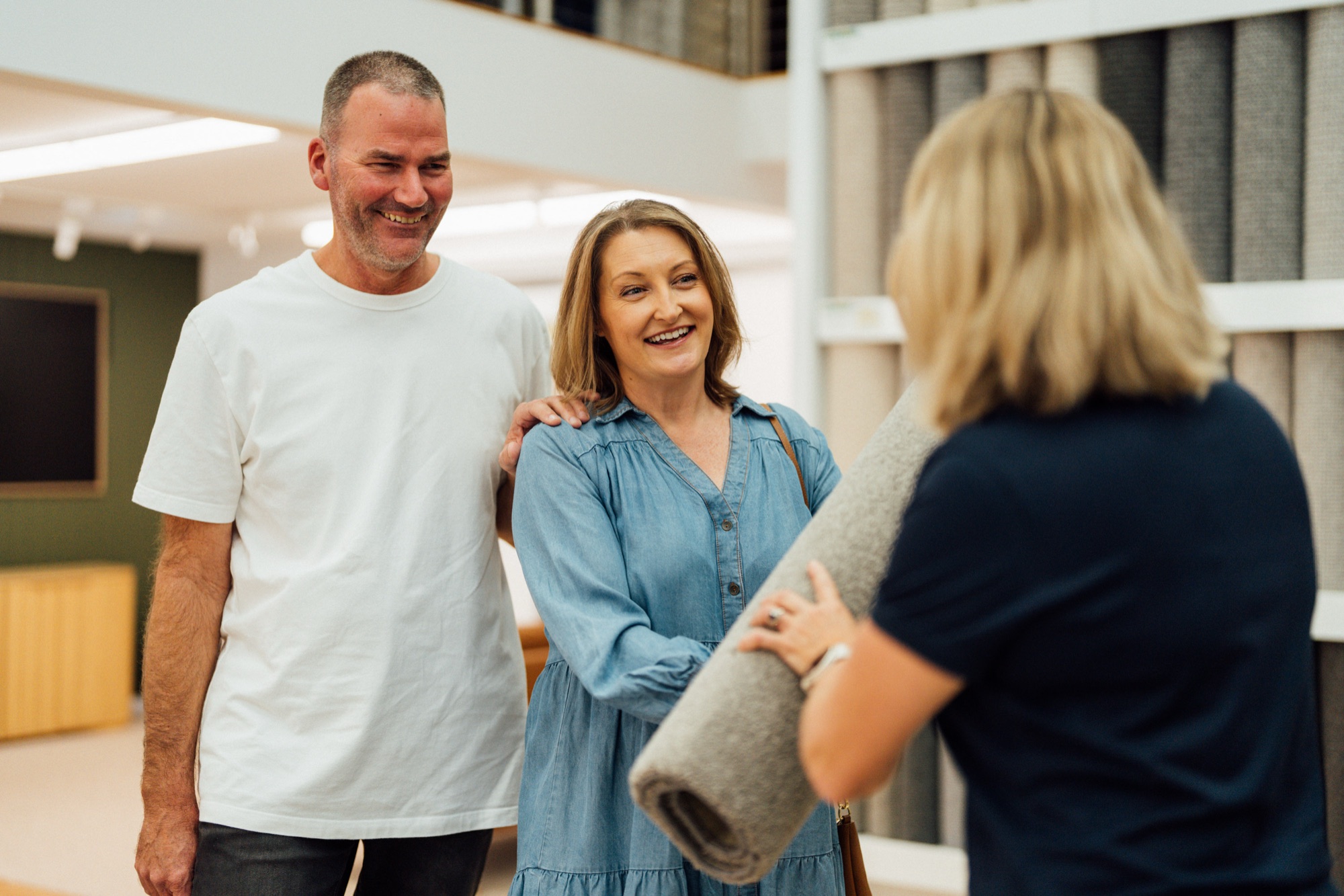 An Andersens consultant handing a rolled carpet sample to two customers in the showroom
