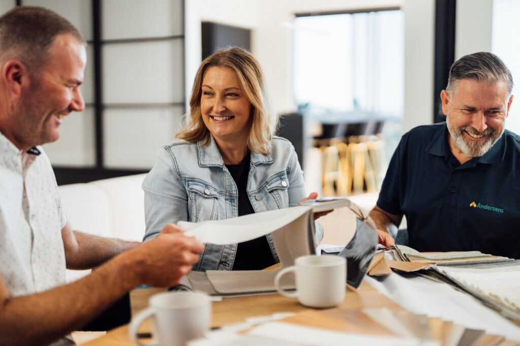 An Andersens consultant showing flooring samples to two customers at their dining table