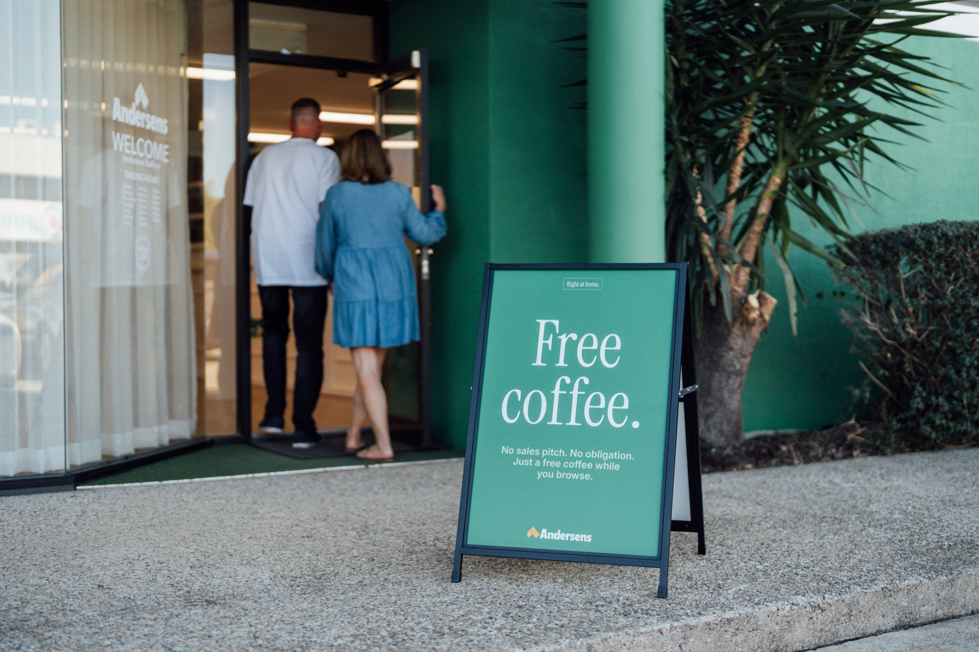Customers walking into an Andersens store past a free coffee sign