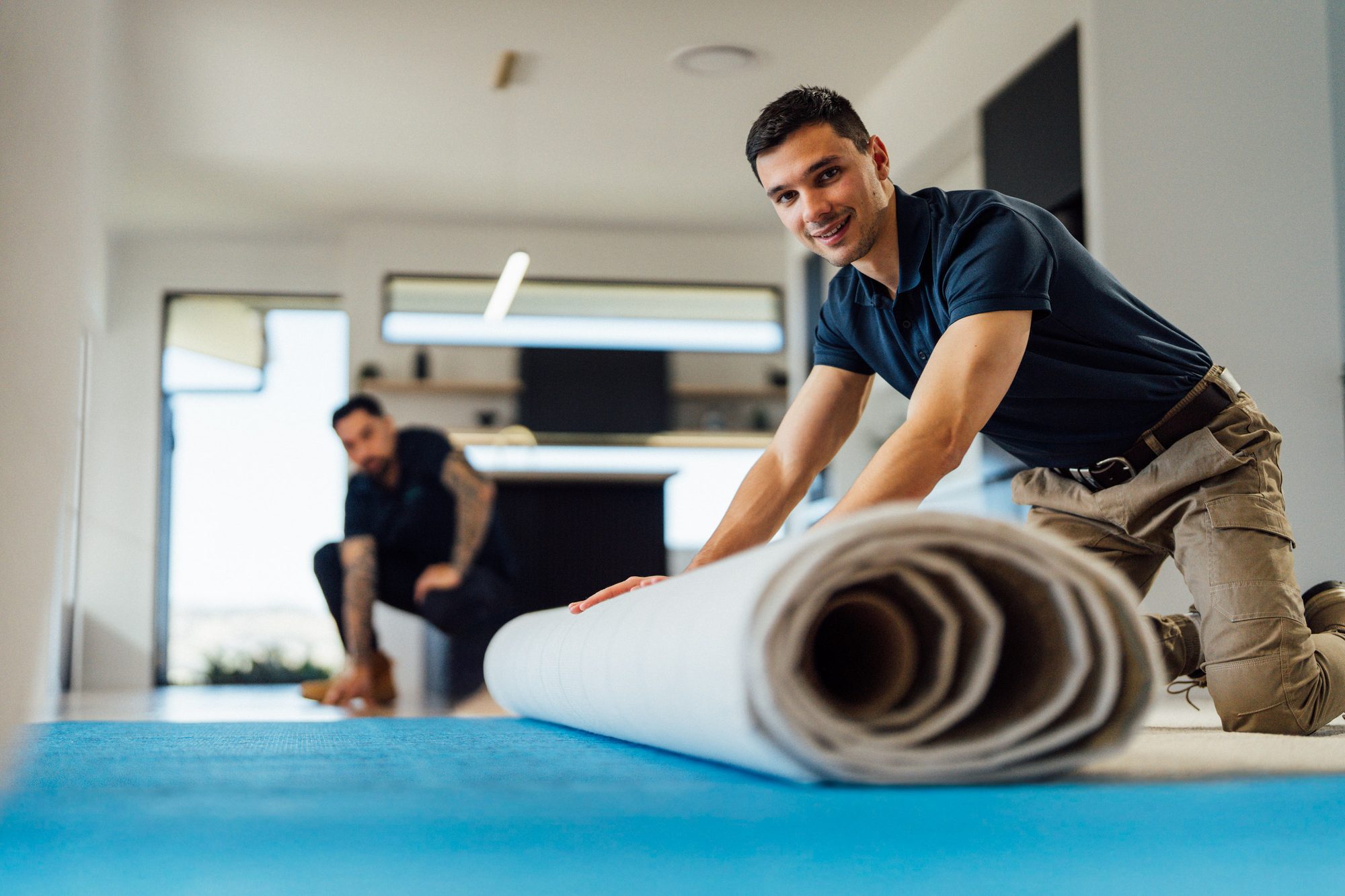 An Andersens installer unrolling new floor covering across a prepared subfloor