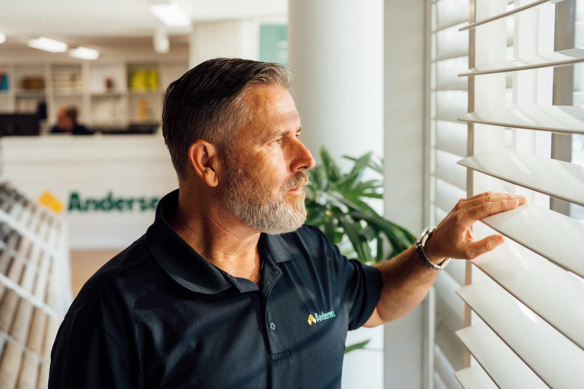 An Andersens staff member looking at the slats of a white venetian blind on showroom display