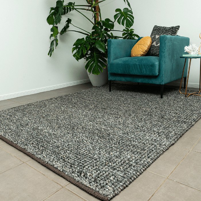 A grey textured wool rug on a pale tiled floor beside an armchair