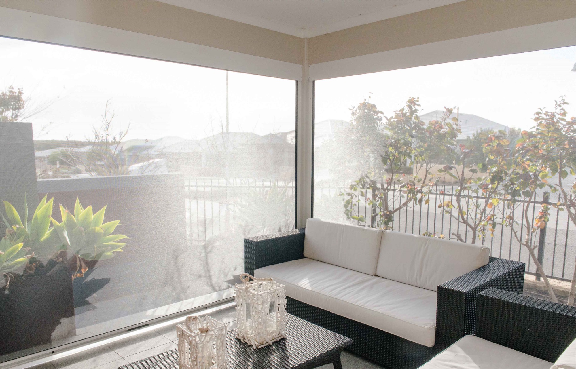 An open-weave exterior screen lowered across a balcony, with the garden still visible through the fabric in daylight