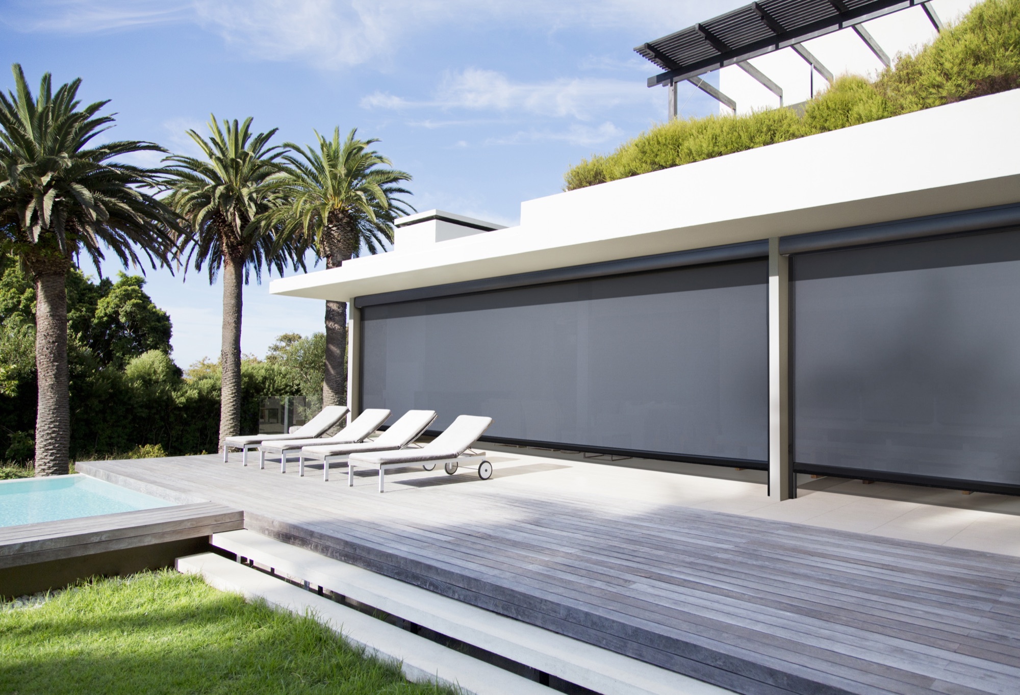 Exterior screens lowered along the length of a timber deck beside a pool