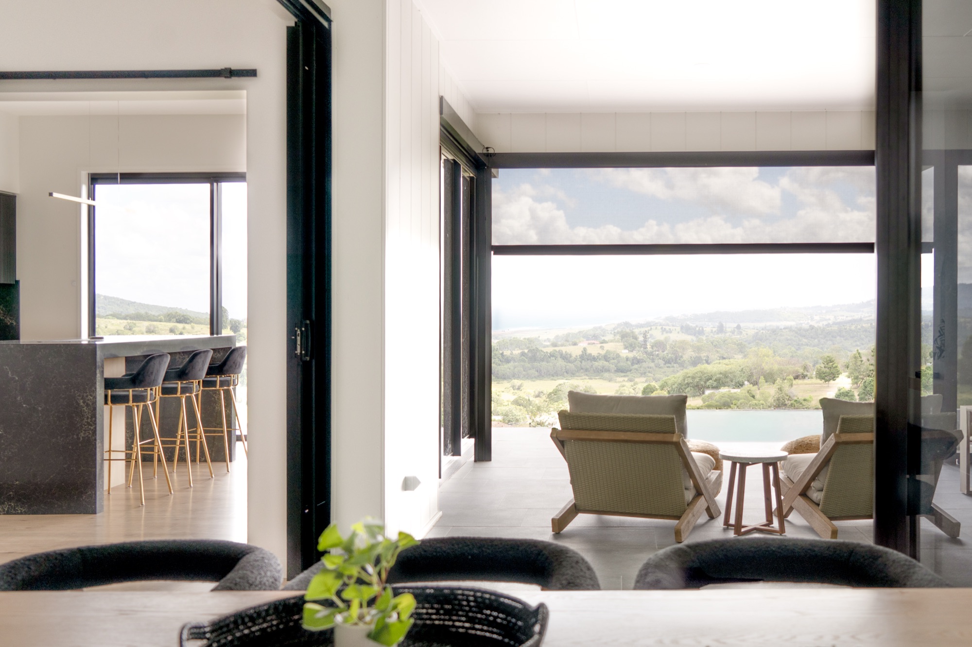 A living area looking out through an open alfresco opening to a rural view, with the exterior screens raised