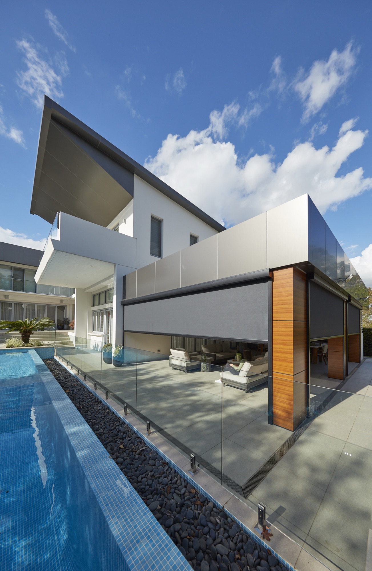 Exterior screens lowered across an alfresco area beside a swimming pool on a clear day