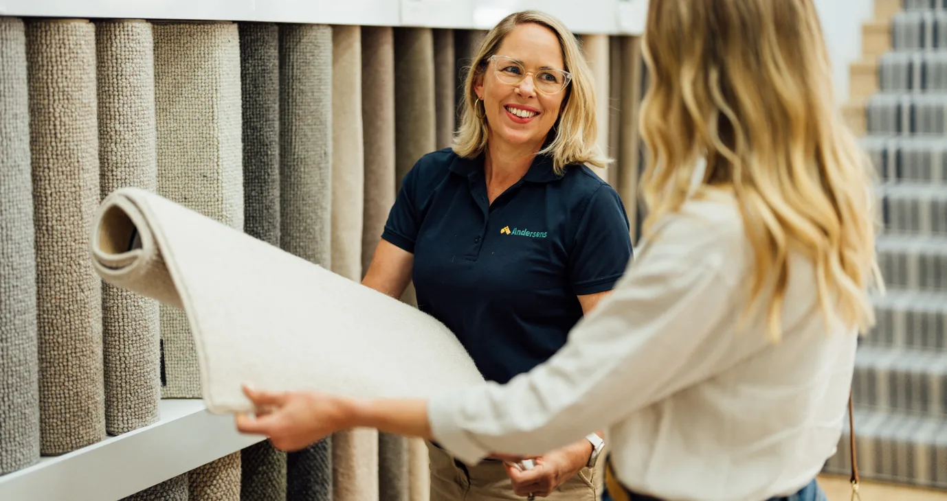 Andersens team member showing a rolled carpet sample to a customer at the showroom sample wall