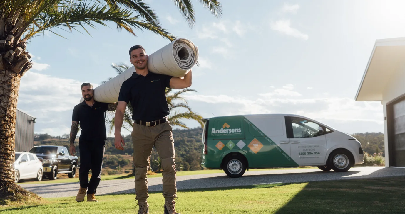 Two Andersens team members carrying carpet beside a branded Andersens van