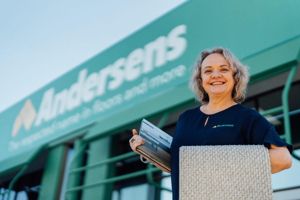An Andersens Centenary team member holding a carpet sample in front of the store sign