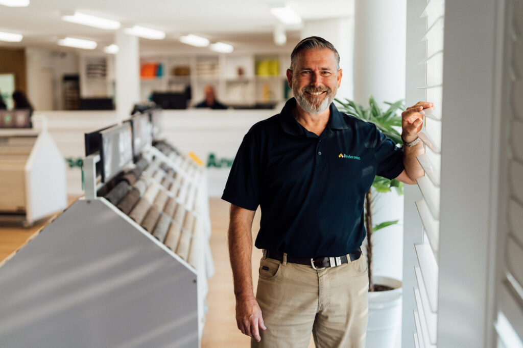 An Andersens Centenary team member smiling beside plantation shutters in the showroom