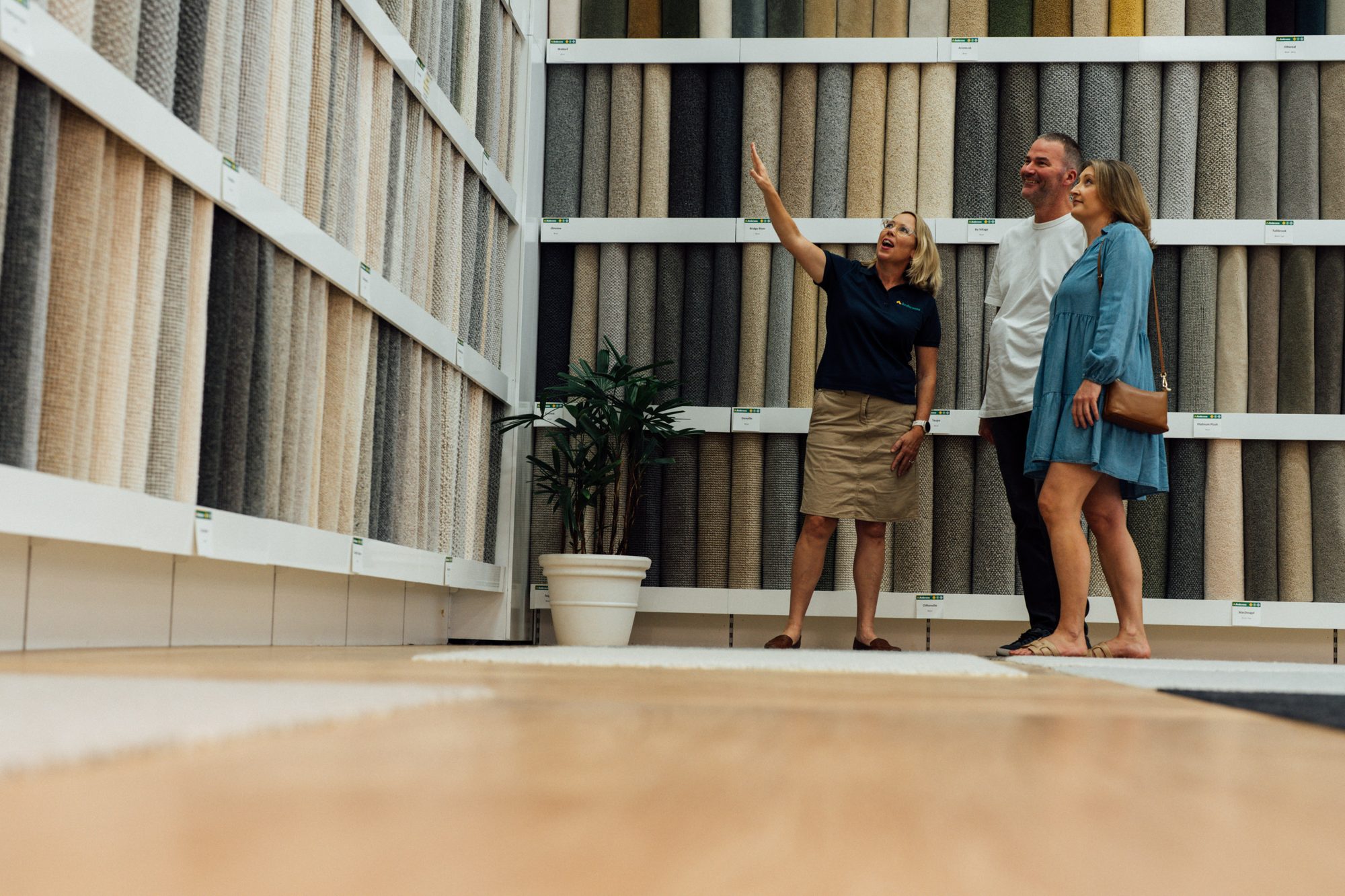 A consultant and a couple in an Andersens showroom beside walls of carpet samples and a timber-look floor
