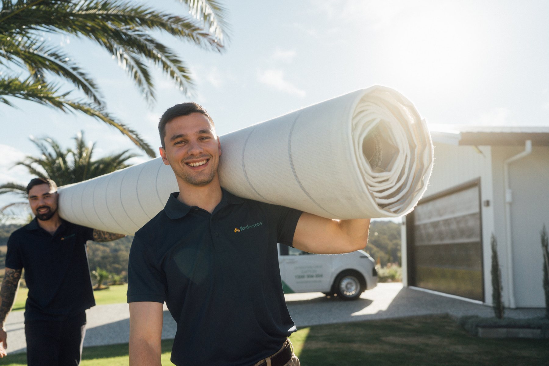 An Andersens team member carrying a roll of carpet on his shoulder outside a home