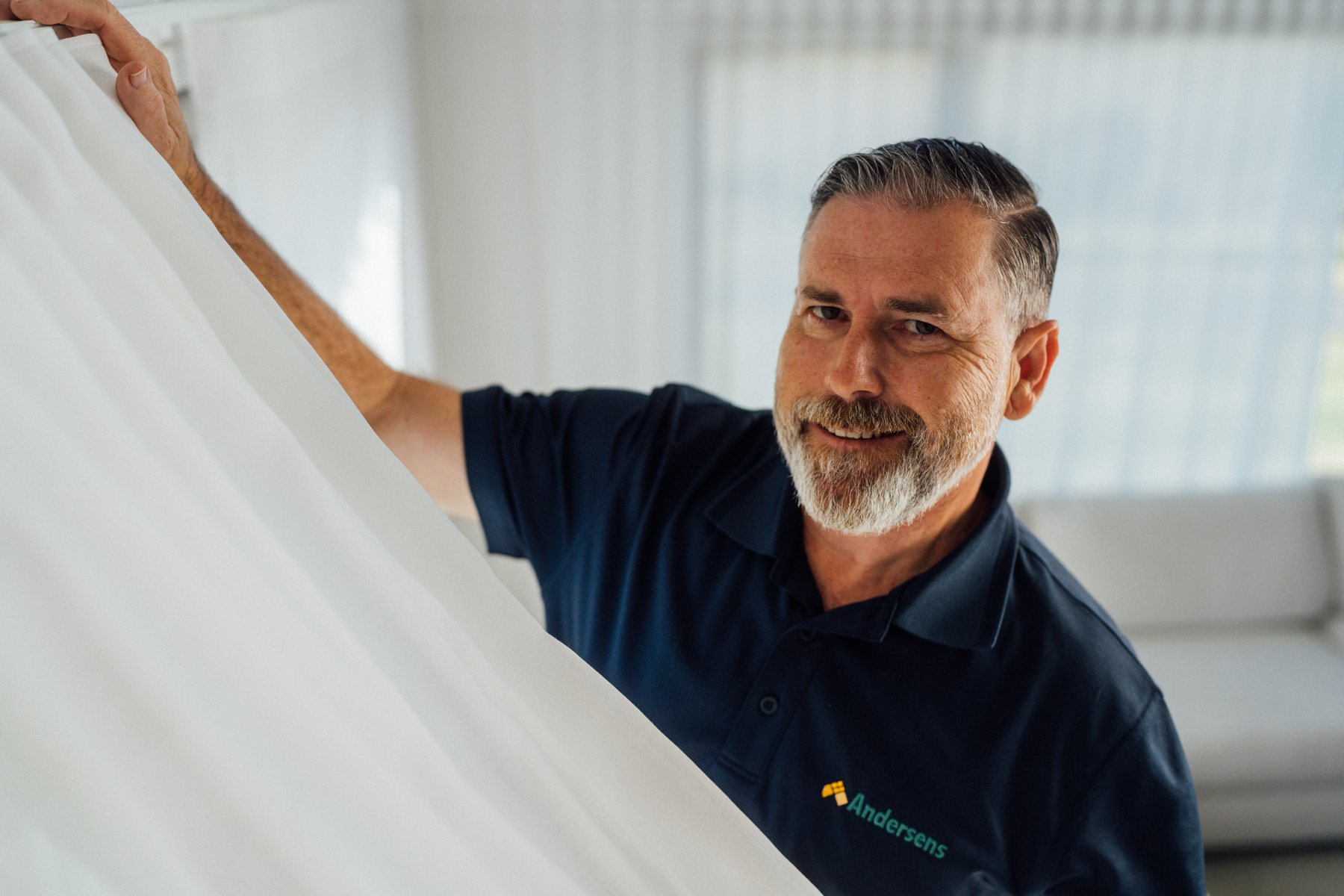 An Andersens team member smiling as he hangs a sheer curtain in a home