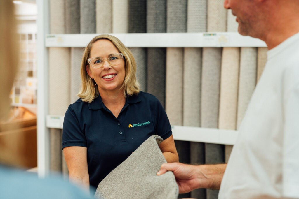 An Andersens consultant smiling while showing a customer a carpet sample in front of the sample wall