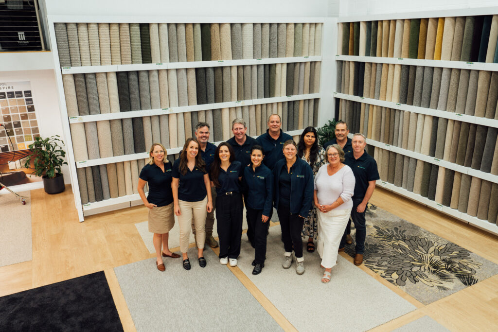 The Andersens Stafford team standing in front of the carpet wall in the showroom